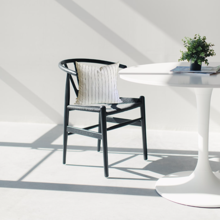 Black and white striped linen pillow cover on a black wishbone chair  sitting at a white tulip table