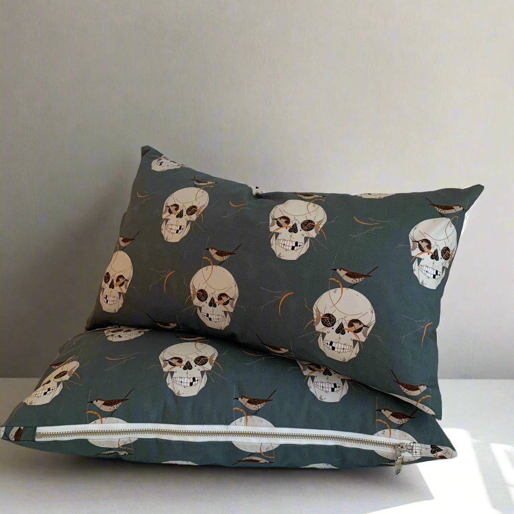 Have fun with your Halloween decor with this playful organic cotton pillow featuring Charlie Harper's spooky Skull and Wren design. The exposed white zipper adds a unique touch against the skulls on a dark grey background. Handcrafted in Canada, this pillow is sure to add some spooktacular charm to your home.

Size 12" x 20" - Down alternative insert with 100% cotton cover included