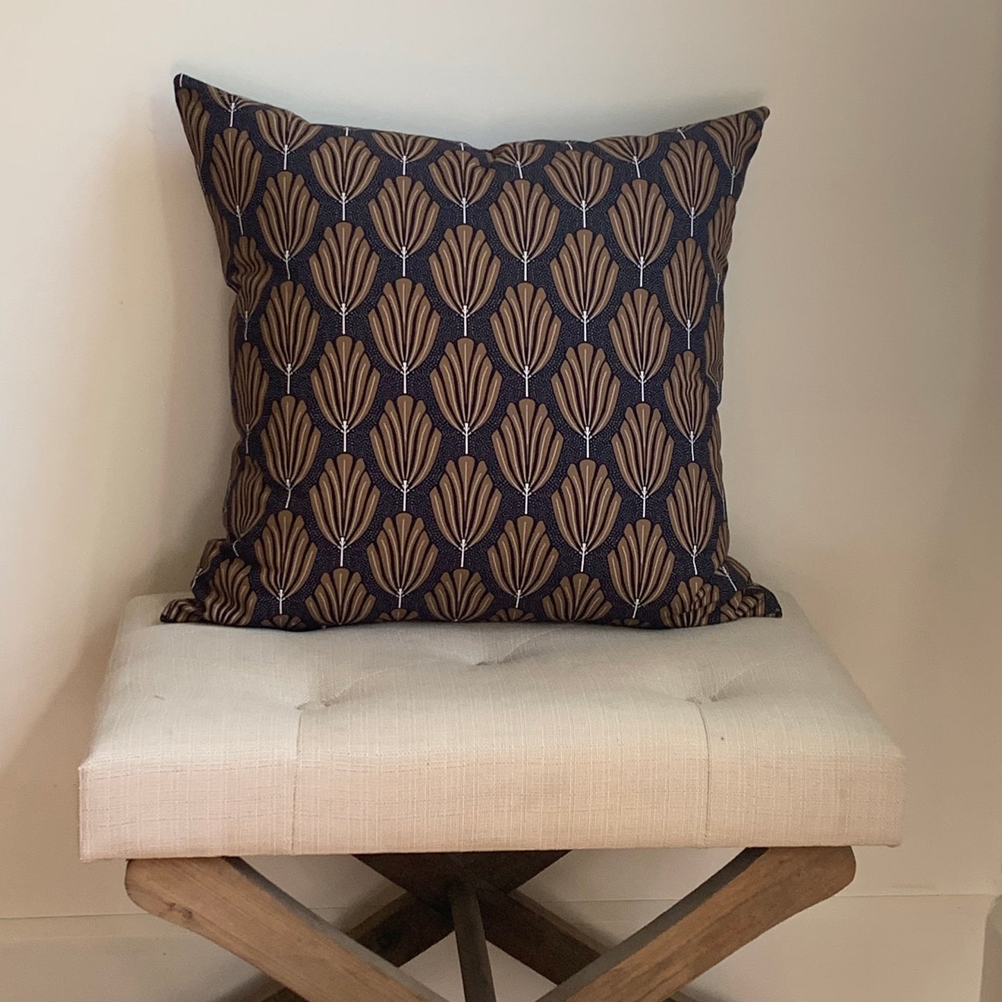 Decorative pillow with geometric pattern on a white cushioned stool against a neutral wall.