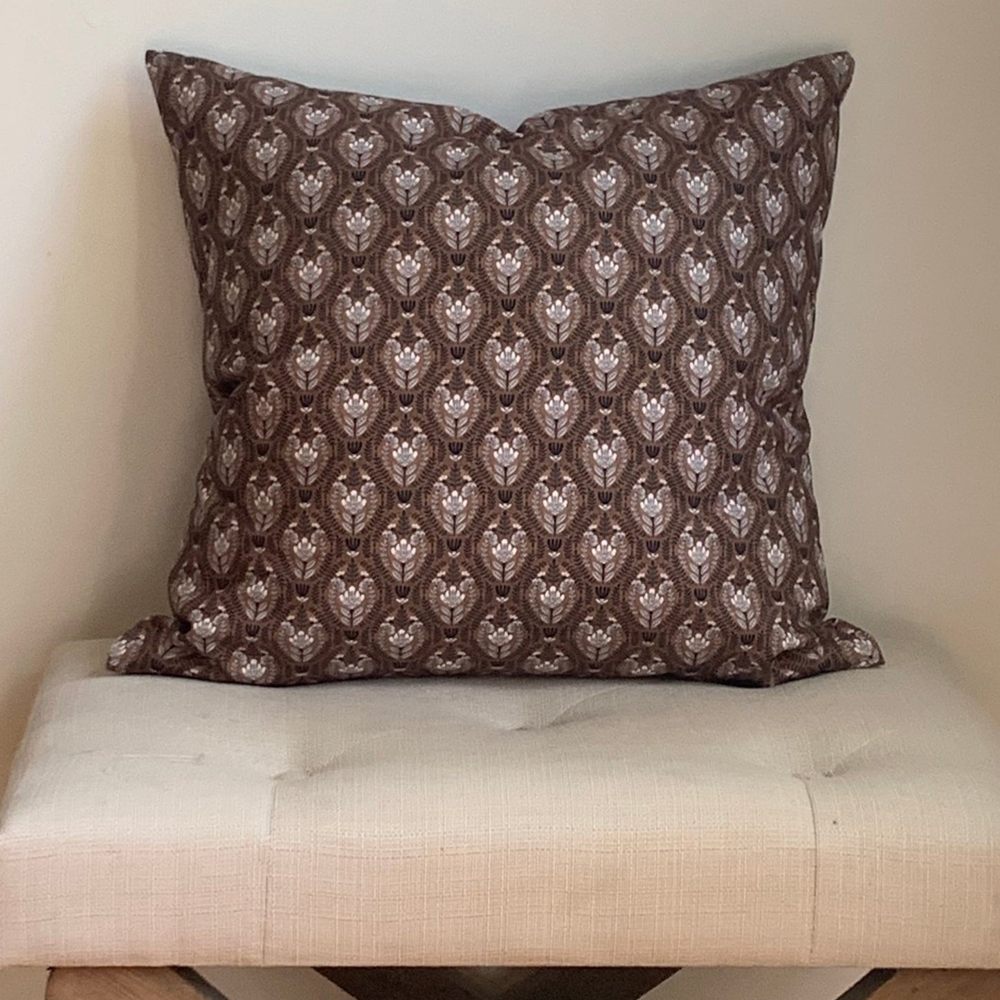 Organic cotton, floral  patterned brown pillow on a beige cushioned stool against a plain wall.