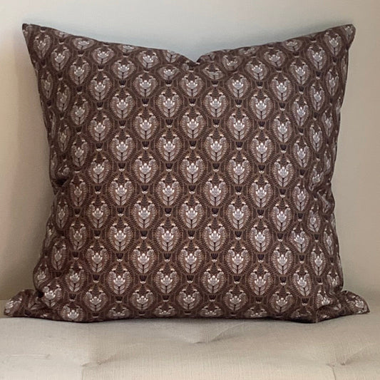 Organic cotton, floral  patterned brown pillow on a beige cushioned stool against a plain wall.