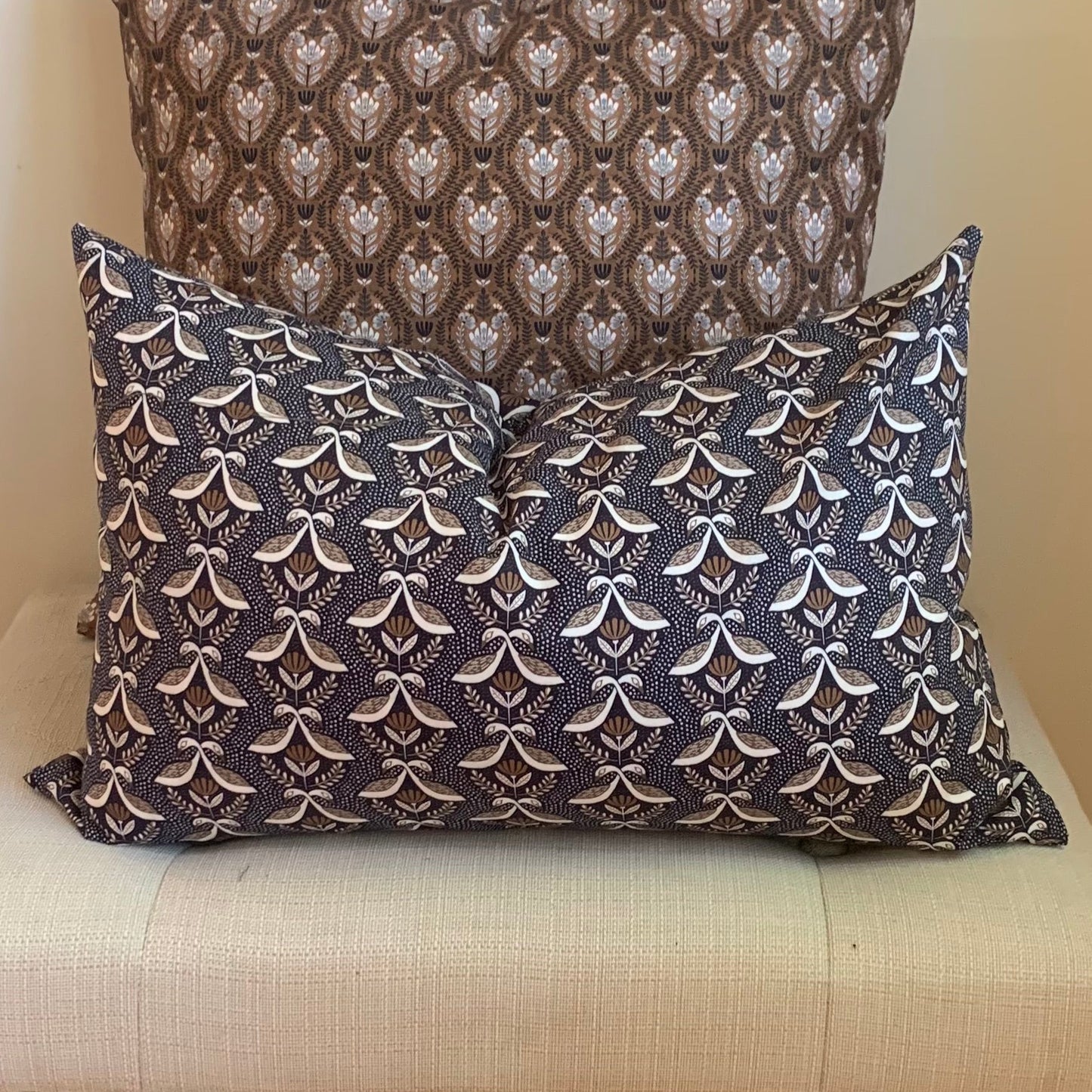 Small goose patterned , organic cotton pillows on a white cushion with a wooden chair in the background.