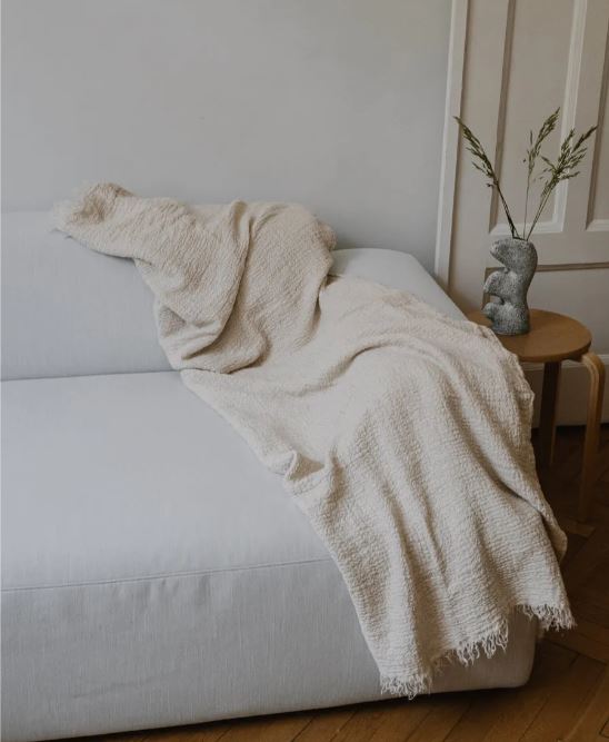 Cream European linen throw draped over a white sofa with a small table and plant in the background.